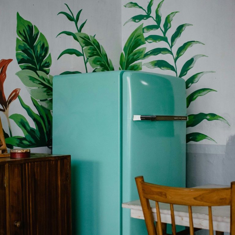 Un frigorífico azul claro junto a un mueble de madera y plantas verdes en la pared.
