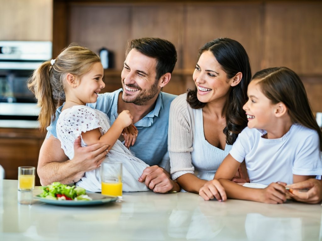 Familia sonriente en la cocina, compartiendo un momento juntos con comida y bebida.